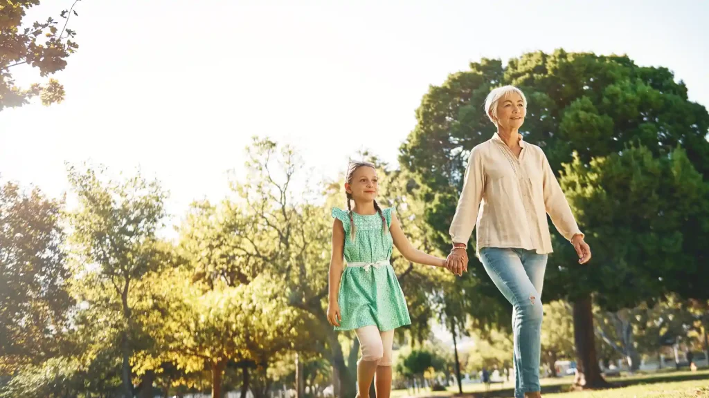 Older woman holding young girl’s hand while strolling in a sunny park